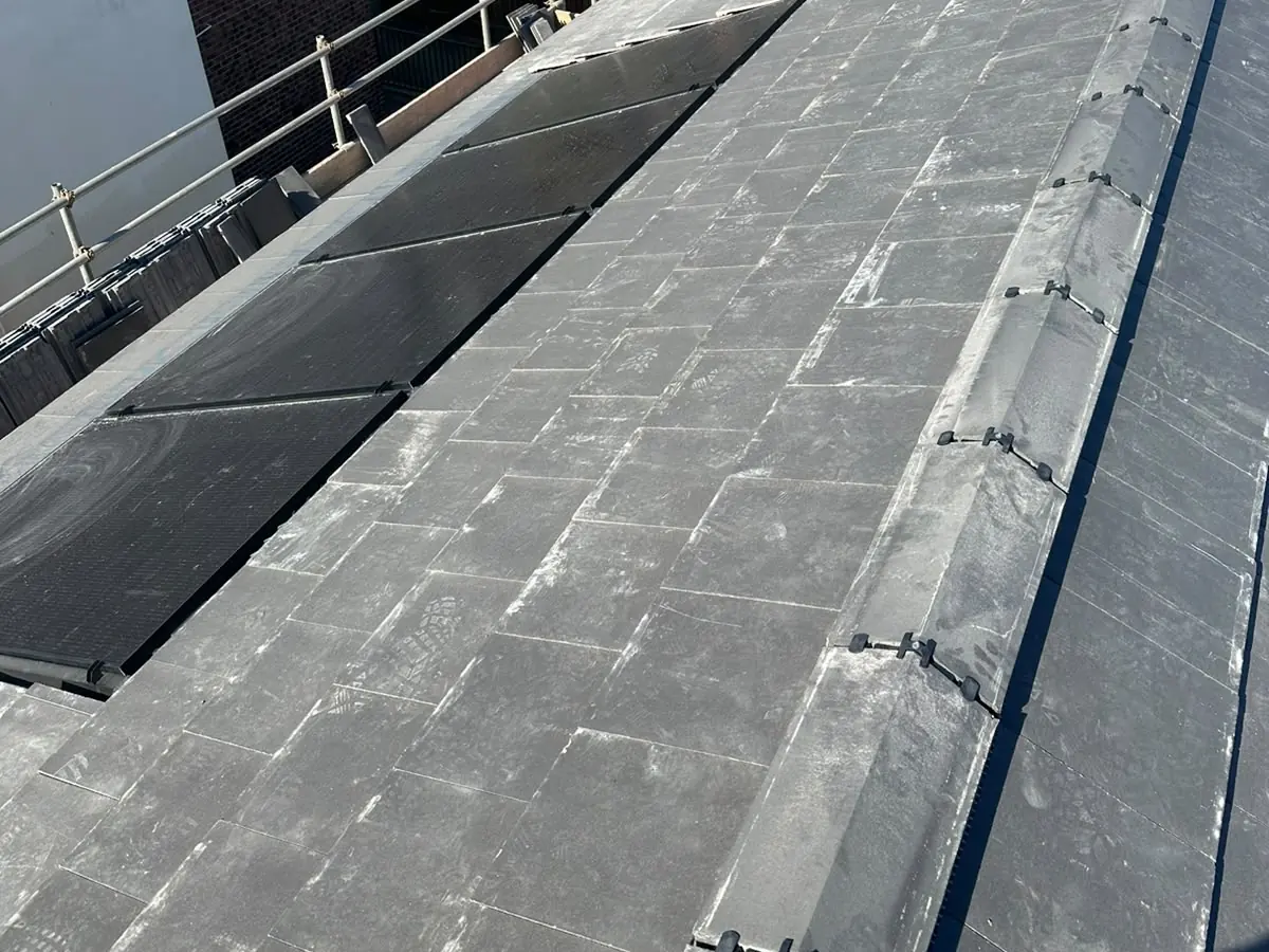 Dry-fixed ridge tiles on a new slate-grey roof with in-roof solar panels and scaffolding